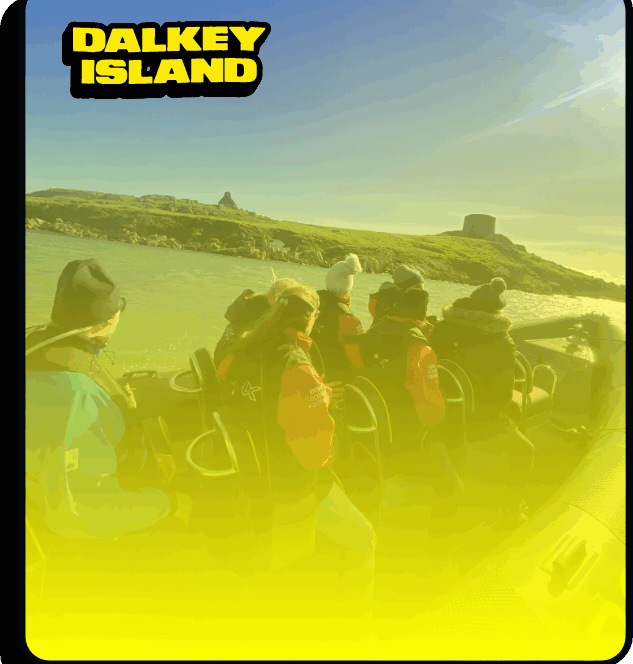 A group of people wearing jackets and hats sit on a boat approaching Dalkey Island, with green hills and a stone tower visible in the background under a clear blue sky. The text DALKEY ISLAND is in the top left corner.