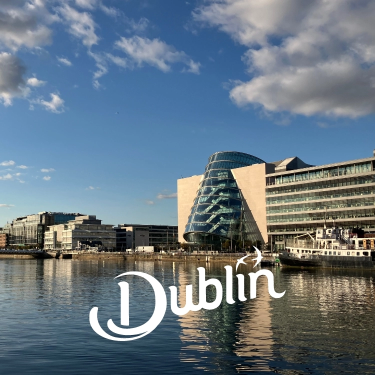 Modern waterfront buildings with a distinctive curved glass structure in the center, reflecting on the calm water. The sky is clear with a few clouds. The text Dublin appears artistically in the foreground.