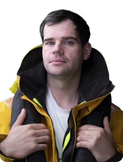 A man with short dark hair wearing a yellow jacket and a life vest stands against a white background, looking confidently at the camera.