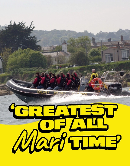 A speedboat with passengers in life jackets moves quickly on the water near houses and trees. Bold yellow text in front reads: "GREATEST OF ALL Mari TIME".