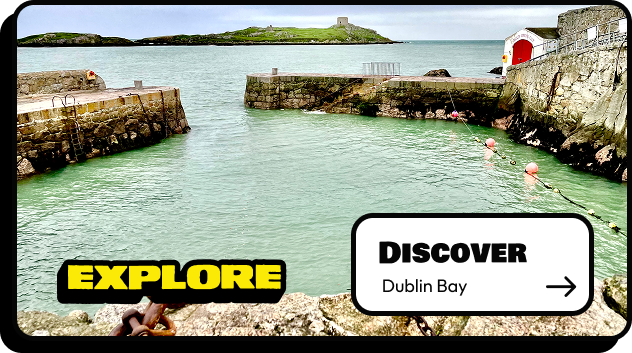 View of a rocky harbor with calm green water, stone piers, and an island with a tower in Dublin Bay. Text reads "EXPLORE" and "DISCOVER Dublin Bay" with an arrow—perfect for your next Dublin boat tour adventure.